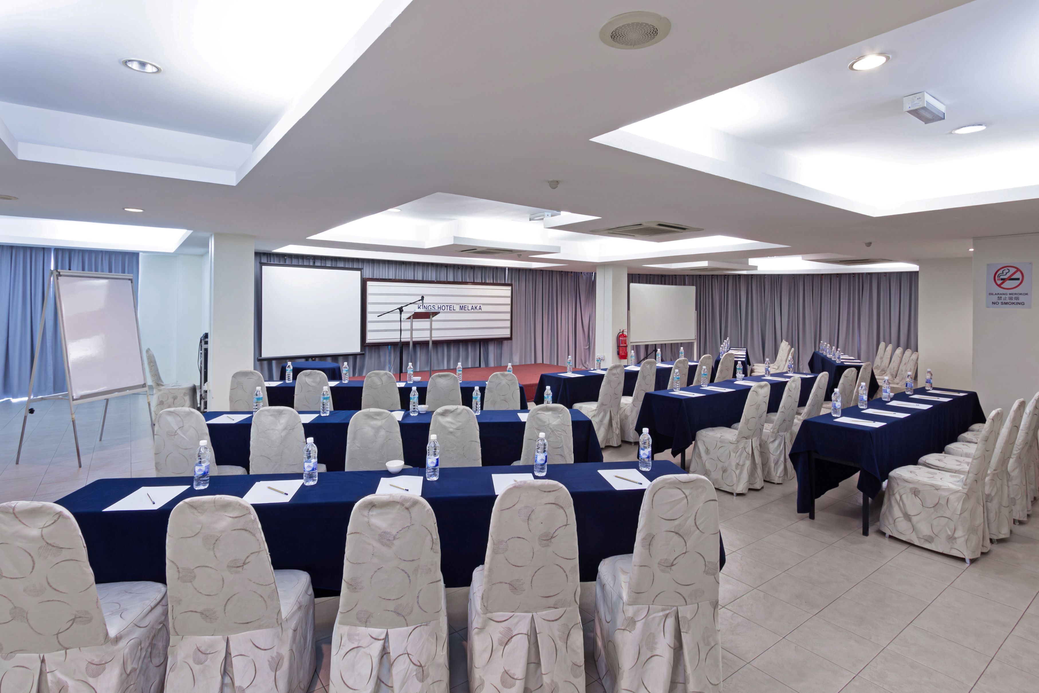 A conference room with multiple tables, chairs, and a presentation screen.