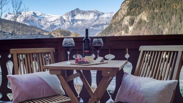 A wooden deck with a table set for two, featuring a bottle of wine and glasses, overlooking a mountainous landscape. - Stylishly renovated, king bed, 120m from telecabin (Les Houches)