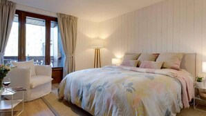 A bedroom with a large bed, a bedside table, a chair, and a window with curtains. - Stylishly renovated, king bed, 120m from telecabin (Les Houches)