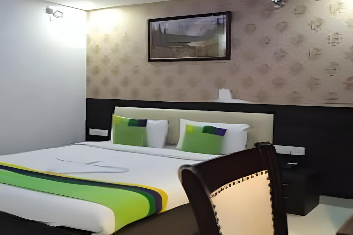 A modern hotel room with a large bed, a headboard, a desk, and a chair.
