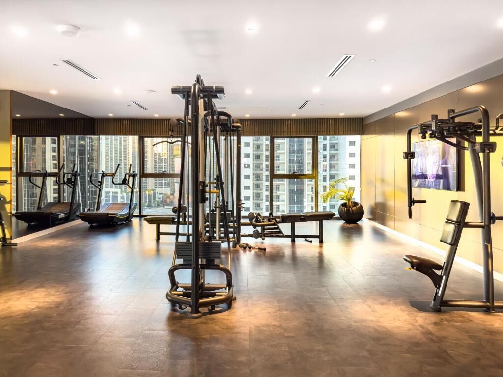 A modern gym with exercise equipment, large windows, and a view of high-rise buildings.