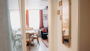Un couloir mène à un espace repas comprenant une table et des chaises, un canapé et un miroir au mur.