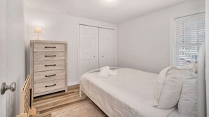 Een slaapkamer met een bed, een dressoir, een kast en een raam met jaloezieën.