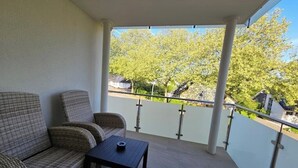Un balcon doté de meubles en osier et d’une petite table, offrant une vue sur un quartier résidentiel avec des arbres et des maisons.