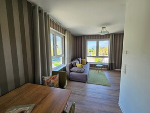 A modern living room with a sofa, a dining table, and a view of the outdoors through large windows. - Fewo Landhaus Schölerberg (Osnabrück)