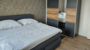 Une chambre à coucher moderne avec un grand lit, une tête de lit sombre, un meuble avec miroir et un lustre.