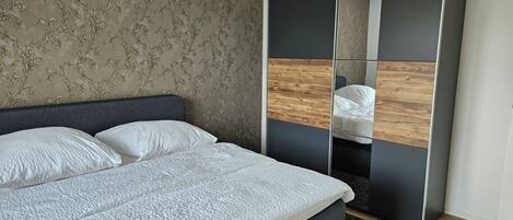 A modern bedroom with a large bed, a dark headboard, a mirror cabinet, and a chandelier.
