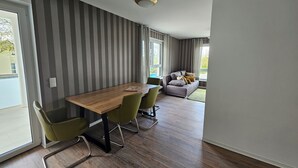 Un salon moderne avec une table à manger en bois, des chaises vertes, un canapé gris et un papier peint à rayures.