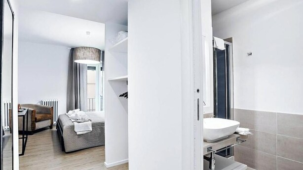 A modern hotel room with a bed, a desk, and a bathroom with a sink and shower. - Luxurious Holiday Home in the Heart of Ancient Rome
 (Roma)