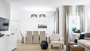 A modern living room with a white sofa, a dining table with chairs, a TV, and a coffee table. - Luxurious Holiday Home in the Heart of Ancient Rome
 (Roma)