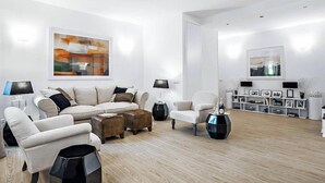 A modern living room with a sofa, armchairs, a coffee table, and a side table. There is a bookshelf with framed pictures and decorative items. - Luxurious Holiday Home in the Heart of Ancient Rome
 (Roma)