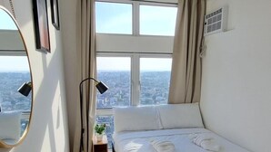 Habitación de hotel con una cama grande, una mesita de noche, un espejo y una ventana con vistas a la ciudad.
