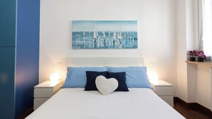 A bedroom with a bed, two bedside tables, a night lamp, a heart-shaped pillow, and a painting of sailboats on the wall. - notaMi - Rainbow Home - CityLife (Milan)