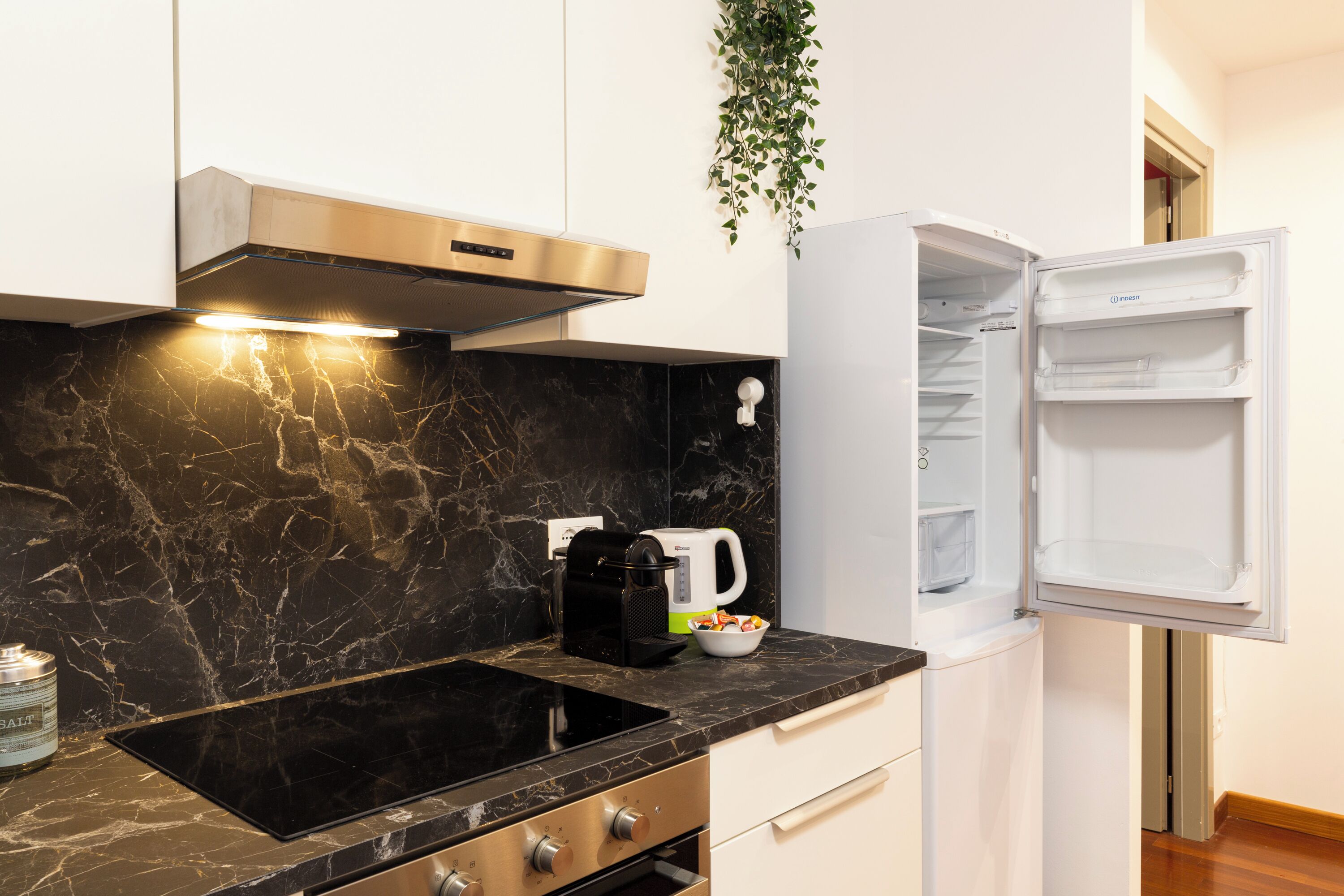 Een moderne keuken met een zwart marmeren aanrecht, een inbouwfornuis, een koffiezetapparaat en een witte koelkast.