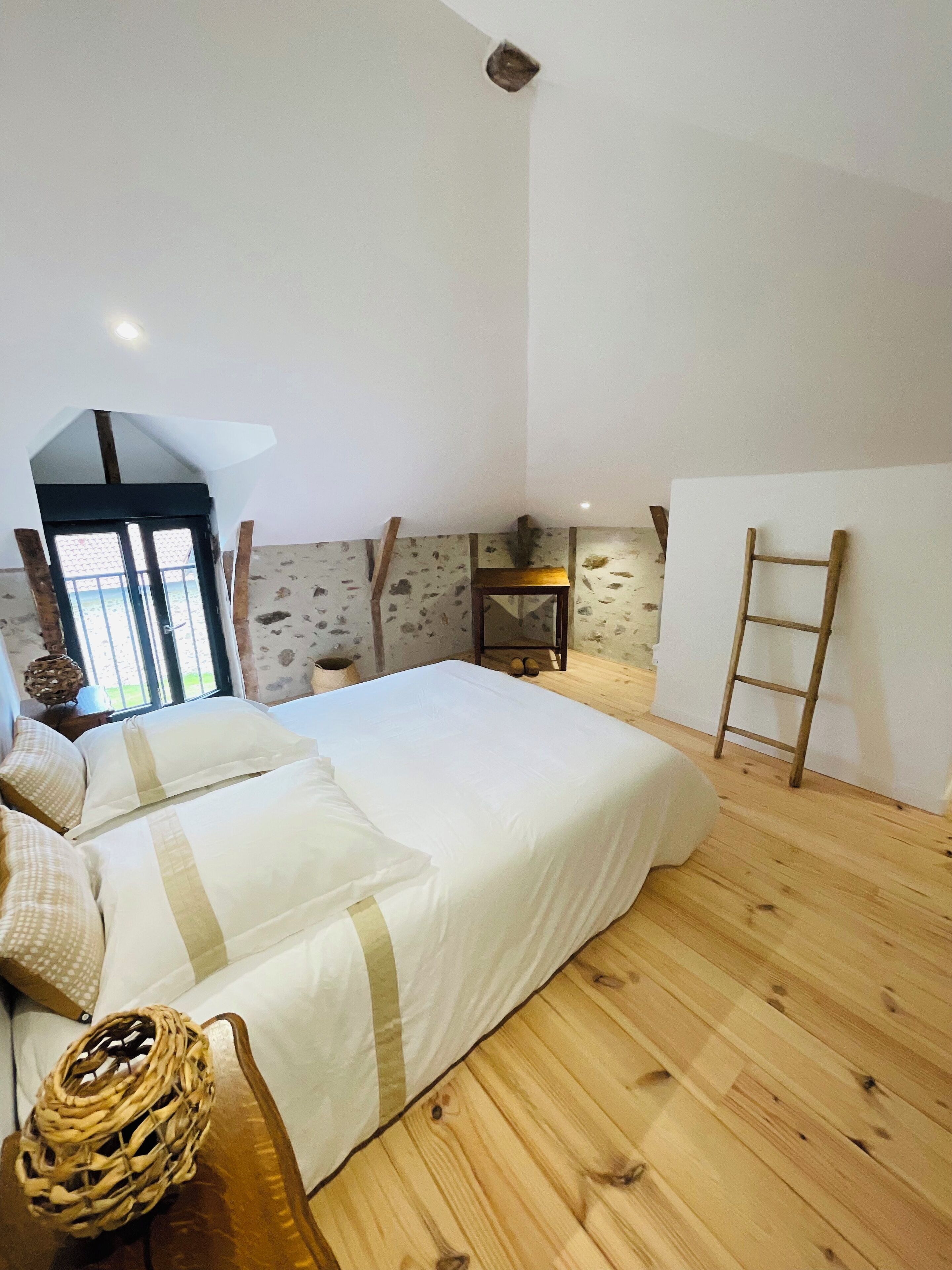 A bedroom with a bed, wooden floor, stone wall, and a ladder.