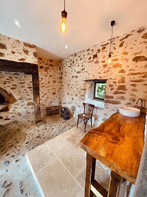 Relax in a cozy space with a wooden table, white sink, and comfortable chair, surrounded by a view of lush greenery.