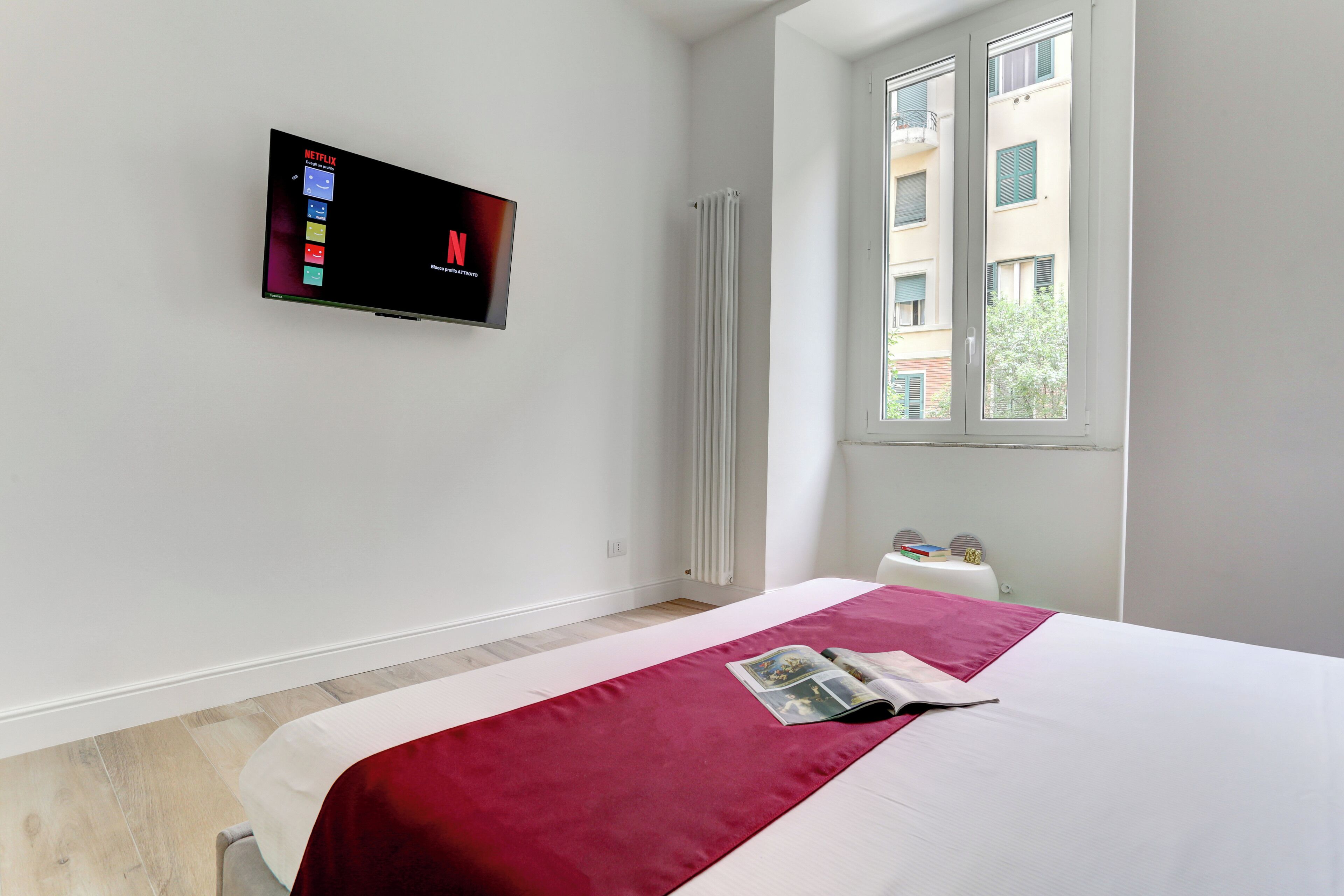 A hotel room with a bed, a TV mounted on the wall, a window, and a radiator.