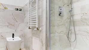 Ein Badezimmer mit Marmorwand, Waschbecken auf Säule, Handbrause und Handtuchhalter.