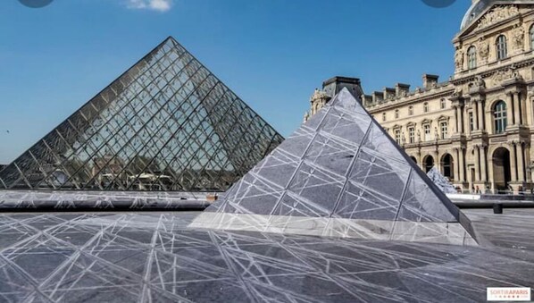 Dos grandes estructuras piramidales frente al Museo del Louvre, con la pirámide de cristal y otra pirámide de cristal en primer plano.