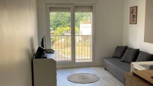A modern living room with a grey sofa, a small white desk, and a round rug. - Disney cocooning 5 minutes from the Park (Coupvray)