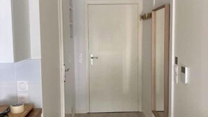 A narrow hallway with a wooden floor, a white door at the end, and a small wooden table with a tape dispenser on it. - Disney cocooning 5 minutes from the Park (Coupvray)