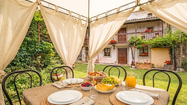 An outdoor dining area with a table set for two, surrounded by greenery, with a building in the background. - Luin Country House Near Stanjel (Komen)