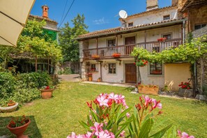 A two-story house with a balcony, surrounded by a well-maintained garden with potted plants and flowers. - Luin Country House Near Stanjel (Komen)