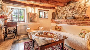 A cozy living room with a stone wall, wooden ceiling beams, a sofa, a coffee table with a tray of pastries, and a vintage sewing machine. - Luin Country House Near Stanjel (Komen)