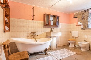 A bathroom with a freestanding bathtub, a wooden chair, a wooden cabinet, a sink, a toilet, and a mirror. - Luin Country House Near Stanjel (Komen)