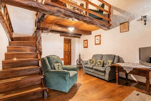 A wooden staircase leading to a loft, a green armchair, a gray sofa, and a wooden table with a TV.