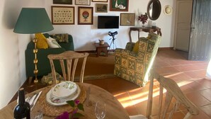 Een eetgedeelte met een ronde tafel gedekt voor twee personen, een groene bank en een aan de muur bevestigde televisie.