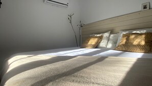 Een slaapkamer met een bed, witte wanden, een houten hoofdeinde en een airconditioning.