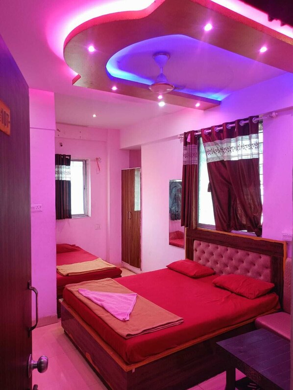 A room with two beds, a ceiling fan, a window with curtains, and a door.
