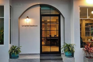 La entrada a Le Cartier Questhouse, con una puerta negra, un accesorio de iluminación encima y dos macetas a cada lado.