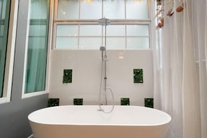 Une salle de bain moderne avec une baignoire sur pieds, une pomme de douche et des carreaux verts décoratifs sur les murs.