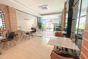 A modern cafe interior with brick walls, wooden flooring, and a mix of table and chair styles. - Le Cartier (Phuket)
