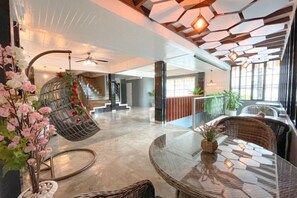 Un vestíbulo espacioso con una silla colgante, una mesa redonda con un centro de mesa de piña y una escalera al fondo.