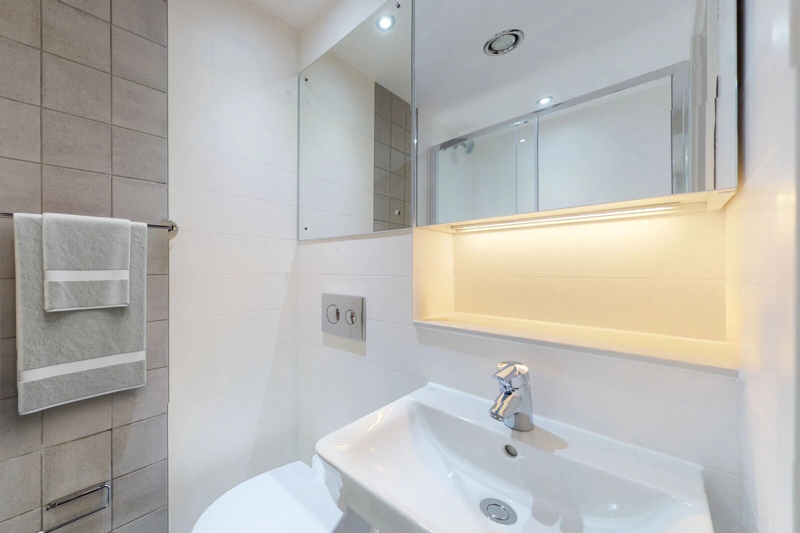 A modern bathroom with a white sink, a mirror, and a towel rack.
