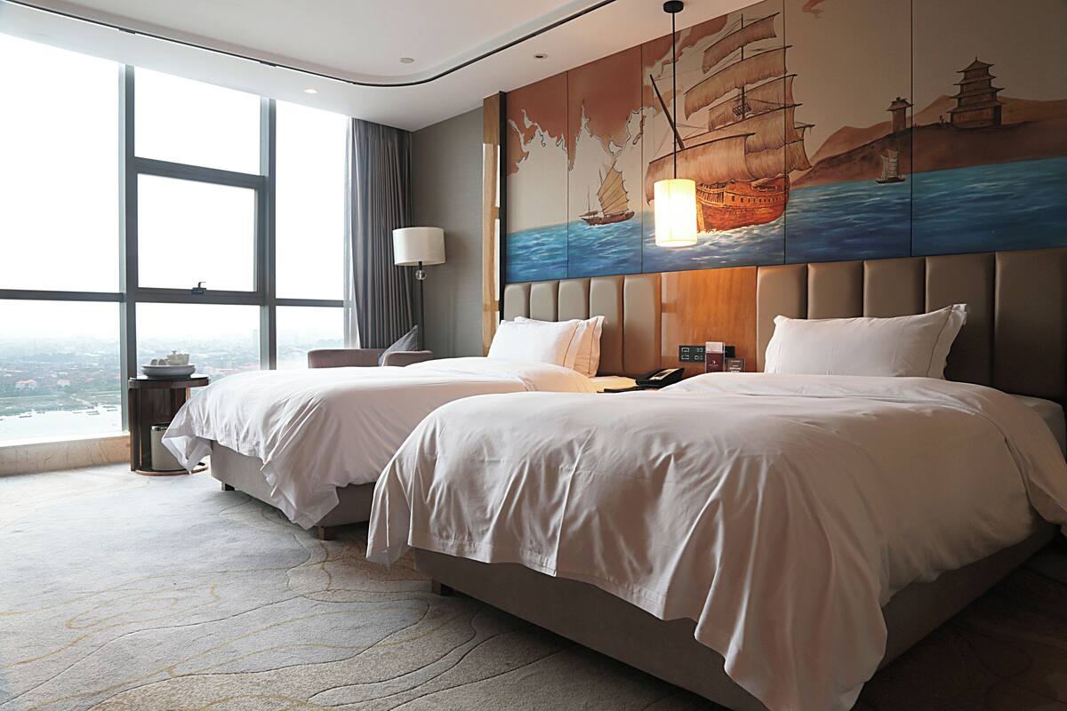 Habitación de hotel con dos camas, un ventanal grande y un mural en la pared.