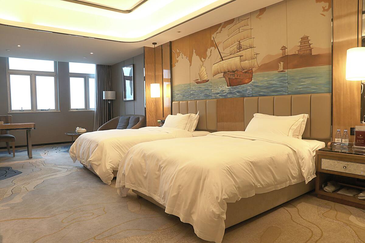 Una habitación de hotel con dos camas, un escritorio, una silla y un ventanal grande.