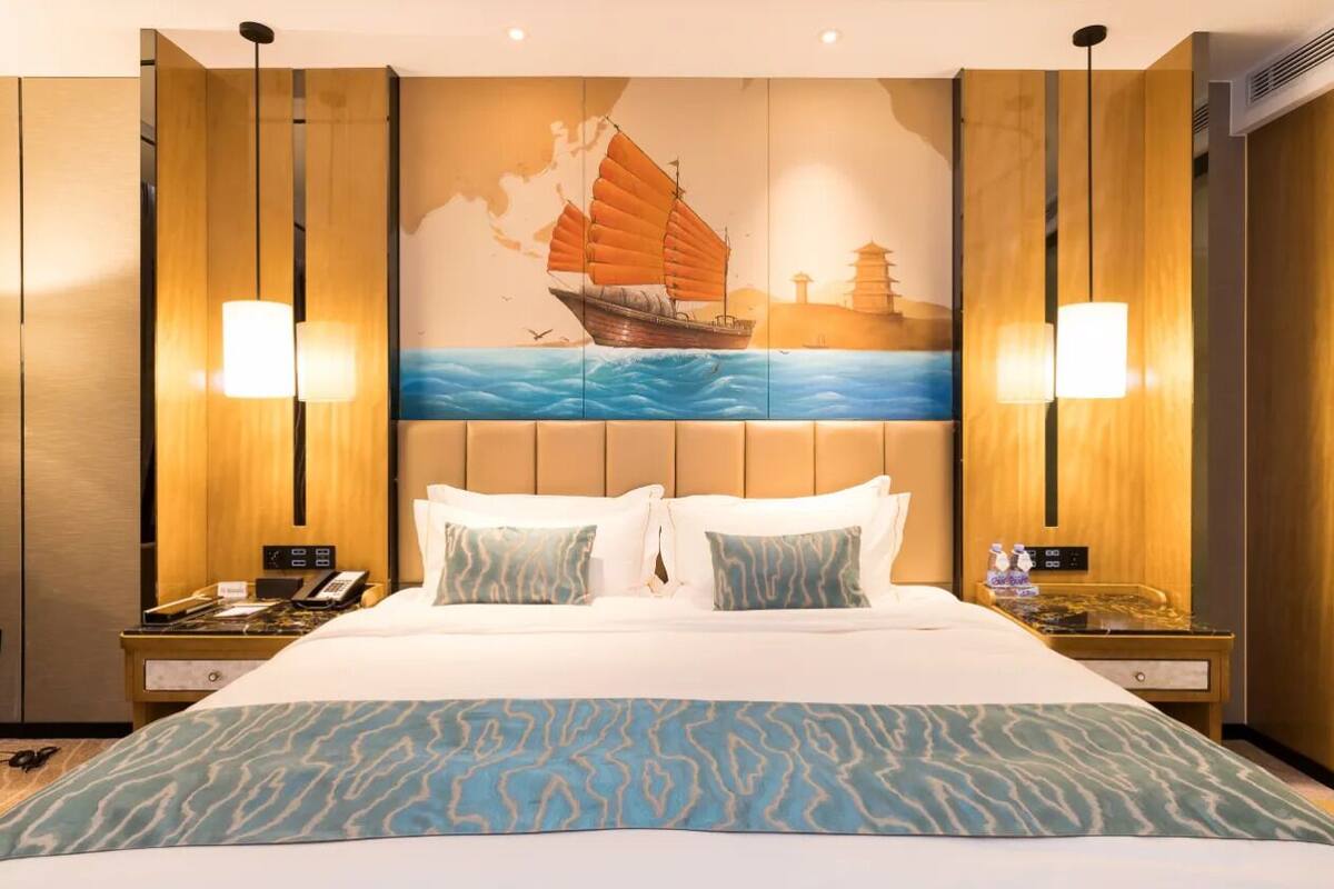 Una habitación de hotel con una cama grande, dos mesitas de noche, un mural náutico de un velero y dos lámparas de pared.