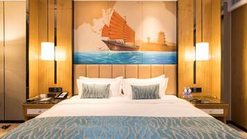 Una habitación de hotel con una cama grande, dos mesitas de noche, un mural náutico de un velero y dos lámparas de pared.