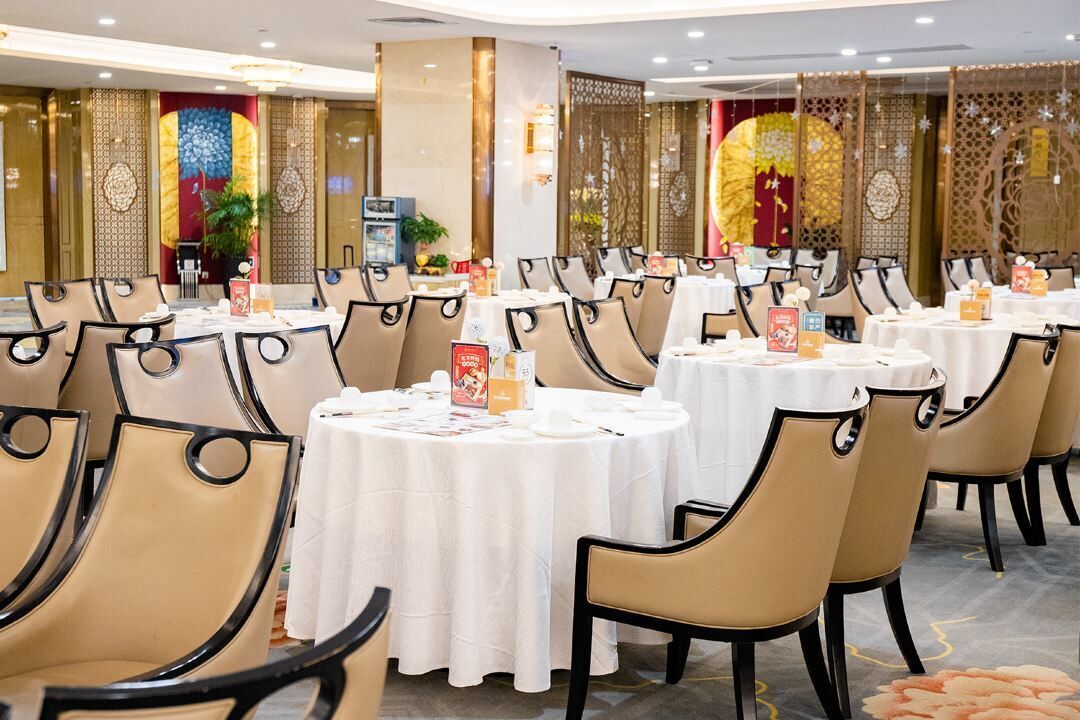 Uma sala de banquetes com mesas redondas e cadeiras, decorada com toalhas brancas e cardápios.