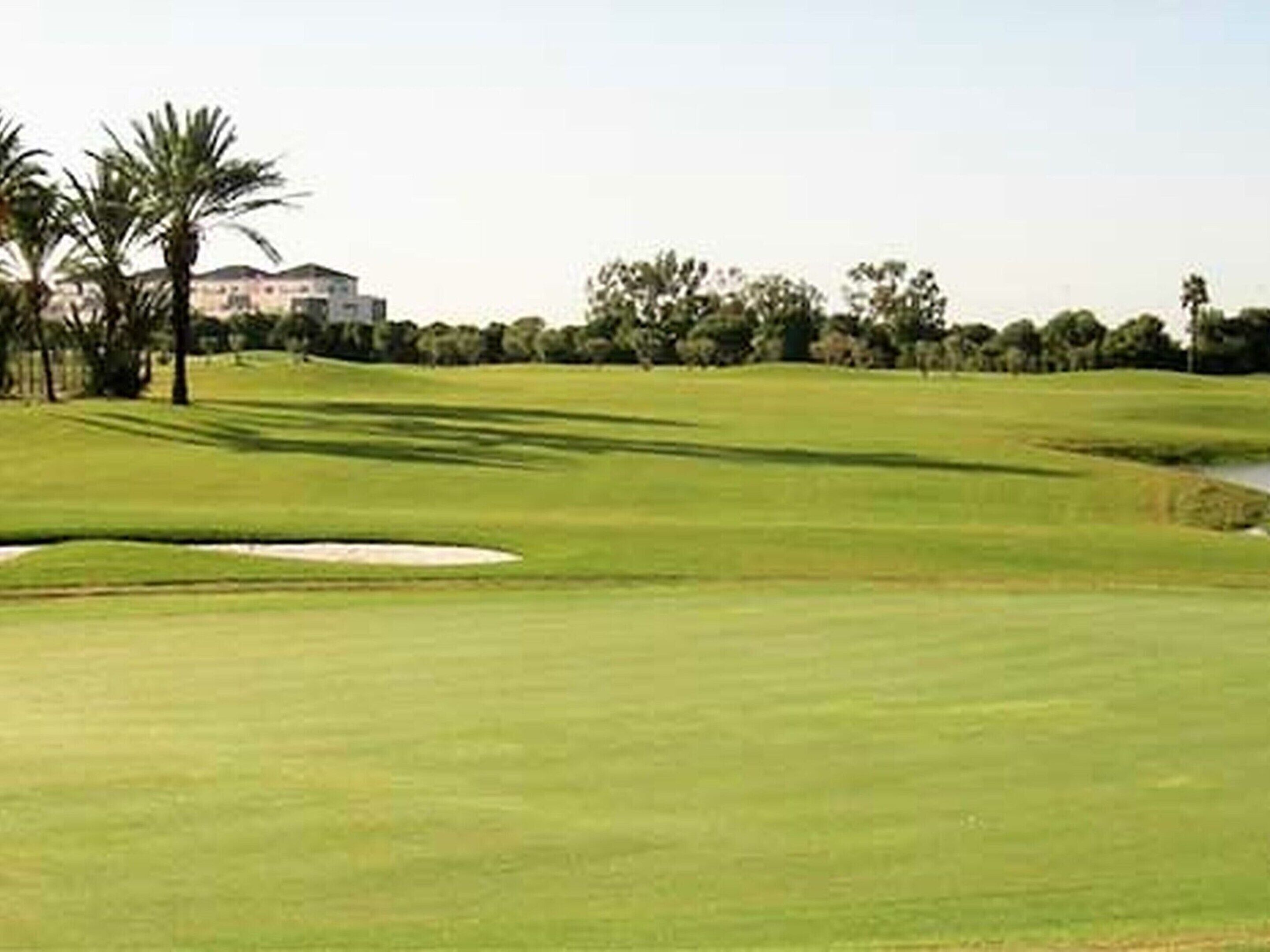 Ein Golfplatz mit Sandbunkern, Palmen und einem Gebäude im Hintergrund.
