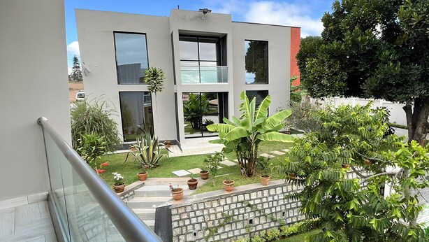 Un edificio moderno con grandes ventanales y un jardín cuidado, con plantas en macetas y un muro de piedra.