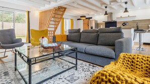 A modern living room with a glass coffee table, a sofa, a yellow armchair, and a staircase. - Charming Cottage with Terrace, Near Beaches, Parking, Wi-Fi, Baby Equipment, and Ping-Pong (Saint-Lyphard)