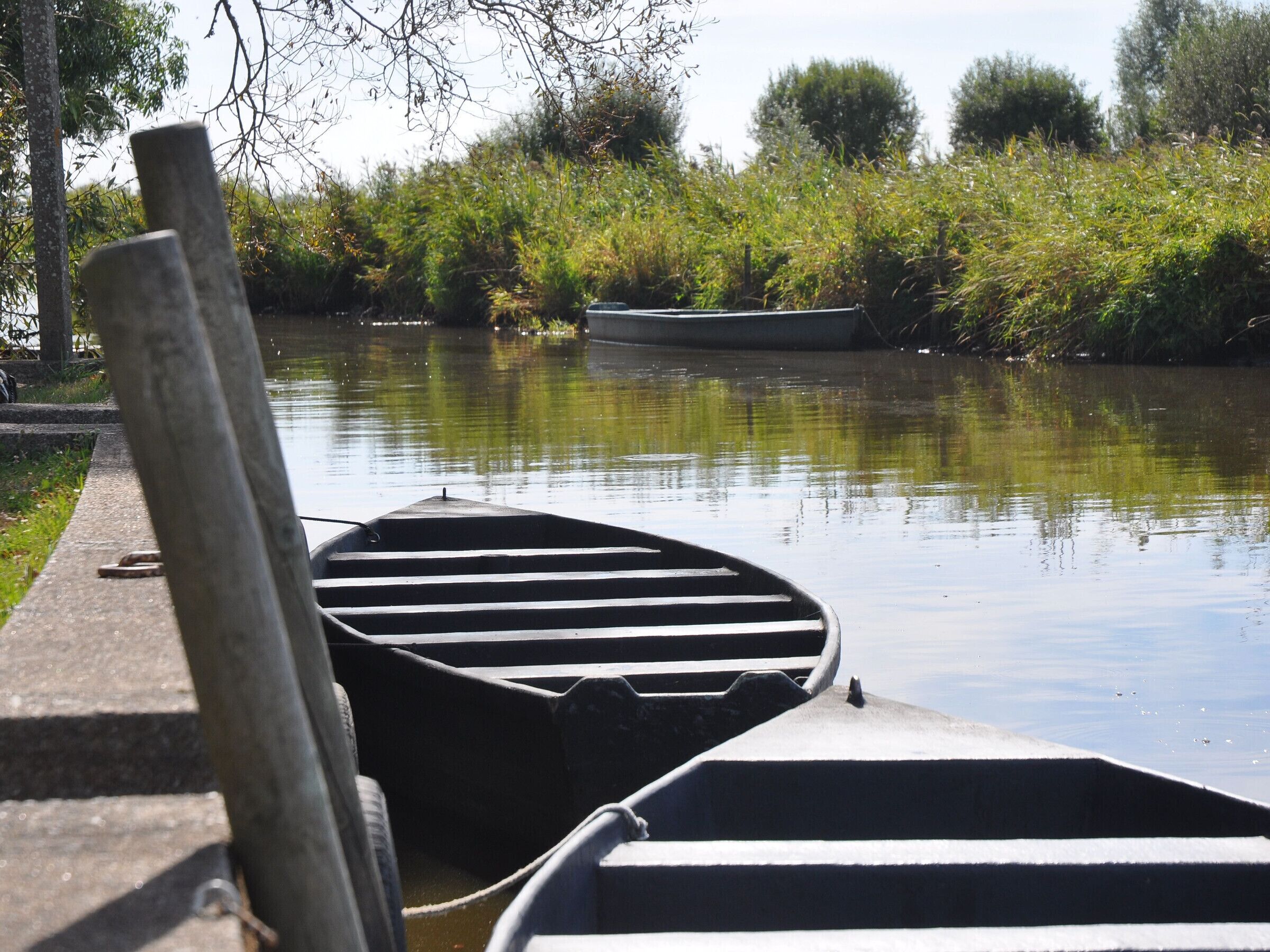 A calm river with two boats docked at the edge of a concrete walkway.