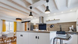 A modern kitchen with white cabinets, a central island, a bar stool, and pendant lighting. - Charming Cottage with Terrace, Near Beaches, Parking, Wi-Fi, Baby Equipment, and Ping-Pong (Saint-Lyphard)