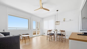 A modern living space with a dining area, a sofa, a ceiling fan, and a TV. - 2-Bedroom Apartment with Beach Access & Private Parking (Roses)