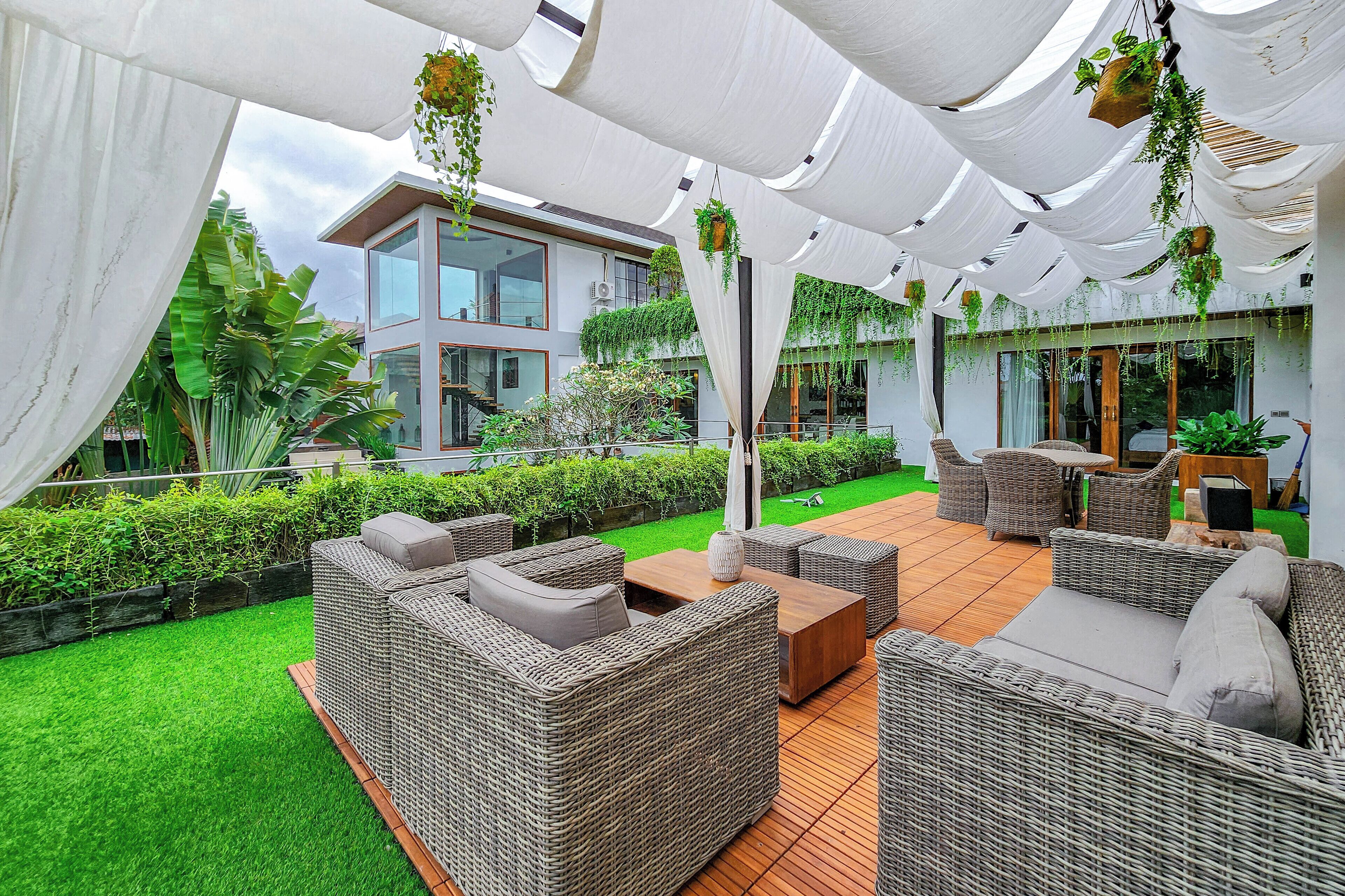 A modern outdoor lounge area with wicker furniture, a wooden deck, and hanging plants.